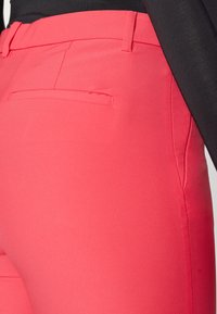 Pink fabric trousers with a smooth texture, featuring a back pocket and tailored fit, complemented by a black top.