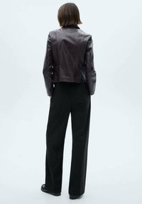 Leren jack in donkerbordeaux, slim-fit vorm met een cropped snit. Gecombineerd met zwarte broek met wijdere pijpen en platte zwarte schoenen, gezien van achteren.