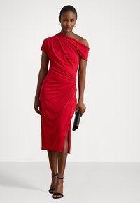 Rochie roșie, plisată, cu un umăr, cu o croială de lungime medie și o fanta laterală, realizată dintr-un material neted. Accesorizată cu o geantă neagră.