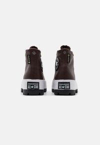 Hnědé vysoké tenisky s gumovými podešvemi, značkou Gore-Tex a černou hvězdou na patě. Mají žluté akcenty a texturovanou látku.