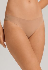 String beige bref et seamless avec une texture lisse, présentant une taille basse et une couverture minimale pour un confort optimal.