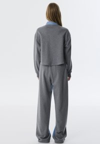 Grijze geknipte sweatshirt met een denim kraag, gecombineerd met grijze tapered broeken. Zachte textuur met een ontspannen pasvorm en ribgebreide manchetten.