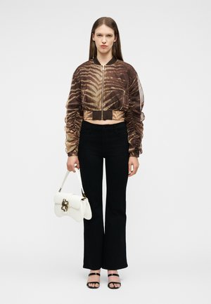 Γυναίκα που στέκεται, φοράει ριγέ καφέ cropped σακάκι, μαύρο παντελόνι, μαύρα σανδάλια και κρατάει μία λευκή τσάντα με χρυσές λεπτομέρειες.