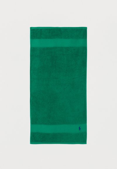 Πράσινη ορθογώνια πετσέτα με υφασμάτινες ρίγες κοντά στις άκρες και μικρό μπλε κεντημένο λογότυπο στην κάτω δεξιά γωνία.