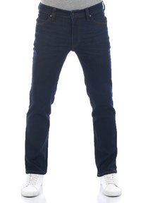 Jeans de mezclilla azul oscuro con corte recto, que presentan un diseño de cinco bolsillos y costuras visibles. Combinados con zapatillas blancas.