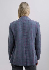 Blazer a cuadros en tela azul con patrón de cuadrícula púrpura. Presenta un cuello clásico, hombros estructurados y un ajuste entallado.