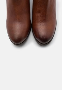 Para wypolerowanych brązowych skórzanych butów pokazanych z góry na białym tle, podkreślająca gładką fakturę i zaokrąglone noski.