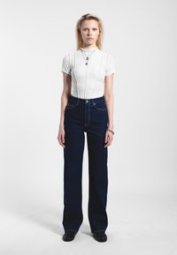 Witte geribde bodysuit met korte mouwen en donkerblauwe high-waisted denim jeans, beide aansluitend, met een minimalistisch ontwerp en een zachte textuur.