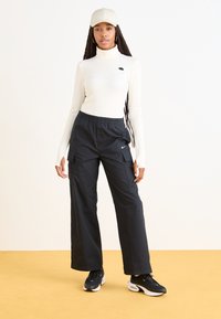 Camisola de gola alta de manga longa em creme, combinada com calças cargo largas pretas com bolsos e um logótipo da Nike. Usada com ténis pretos e um boné.