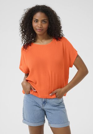 Orange short-sleeve top made of textured fabric, paired with high-waisted denim shorts. The outfit features a relaxed fit and round neckline.