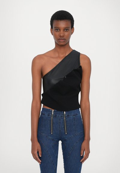 Haut asymétrique à une épaule en simili cuir noir et tissu doux, associé à un jean taille haute bleu avec des zips avant doubles et des détails de coutures.