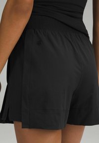 Schwarze Sportshorts mit einem gerippten Bund, die eine lockere Passform und seitliche Schlitze für mehr Bewegungsfreiheit bieten. Dezentes Logodesign sichtbar.