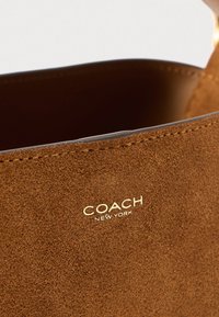 Barna szarvasbőr bevásárlótáska arany "COACH NEW YORK" logóval, sima belsővel, nyitott felső résszel és varrás nélküli részletekkel.