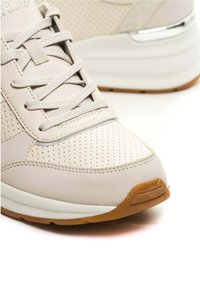 Sneaker beige con tomaia in pelle perforata, lacci piatti e suola intermedia bianca. Presenta una suola in gomma e un accento argentato sul tallone.