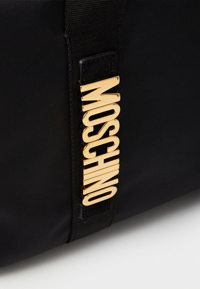 Sac en nylon noir avec une étiquette logo en métal doré bien en vue portant l'inscription "MOSCHINO", au design élégant et à la texture lisse.