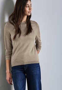 Pull beige avec un col rond, des poignets et un ourlet �à côtelage, associé à un jean bleu foncé. Texture douce, design décontracté.