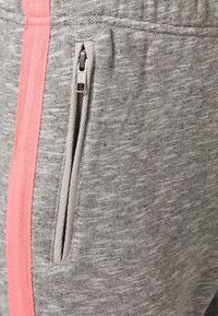 Graue Sweatpants mit glatter Textur zeigen einen pinken Streifenakzent an der Seite und eine Reißverschlusstasche.