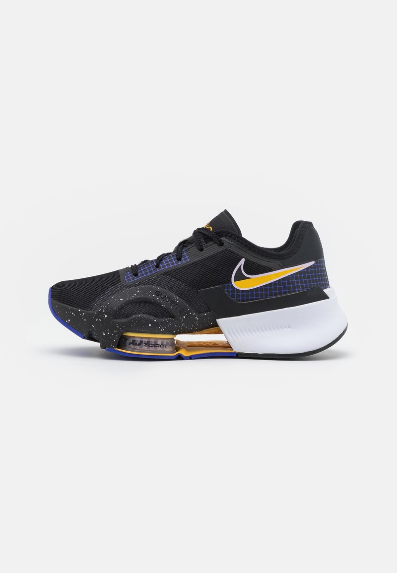 Chaussure de running Nike noire et blanche avec des accents jaunes, semelle à coussinet d'air visible, détails en quadrillage bleu et semelle intermédiaire mouchetée sur fond uni.