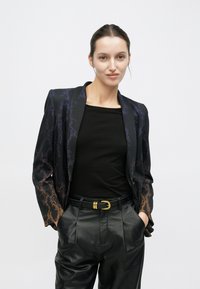 Blazer noir à motif serpent, avec des accents violets et orange, assorti à un haut noir et un pantalon taille haute en similicuir.