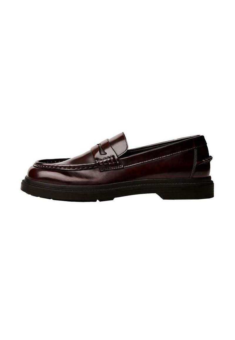 Brown leather loafers with a rounded toe, detailed stitching, and a rubber sole. Features a decorative strap, smooth texture.