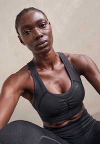 Sujetador deportivo gris oscuro con escote en forma de U, tejido texturizado, copas ligeramente acolchadas y banda elástica; combinado con leggings a juego.