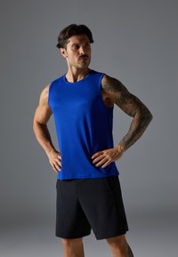 Top desportivo sem mangas azul, feito de tecido suave, combinado com calções pretos. Apresenta um decote redondo e um corte descontraído.