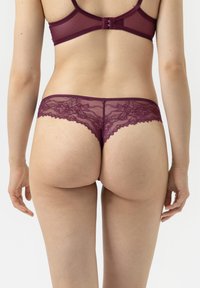 Burgundy spetsunderkläder med flikiga kanter, genomskinligt tyg, blommönster och låg midja, sedd från baksidan.