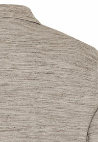 Nærbillede af en beige og brun tekstureret skjorte, der viser øvre ryg og kraveområde.