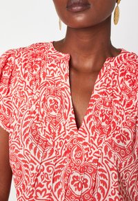 Top a righe rosse e bianche con design plissettato e scollatura a V. Presenta maniche corte a palloncino e un tessuto di cotone testurizzato.
