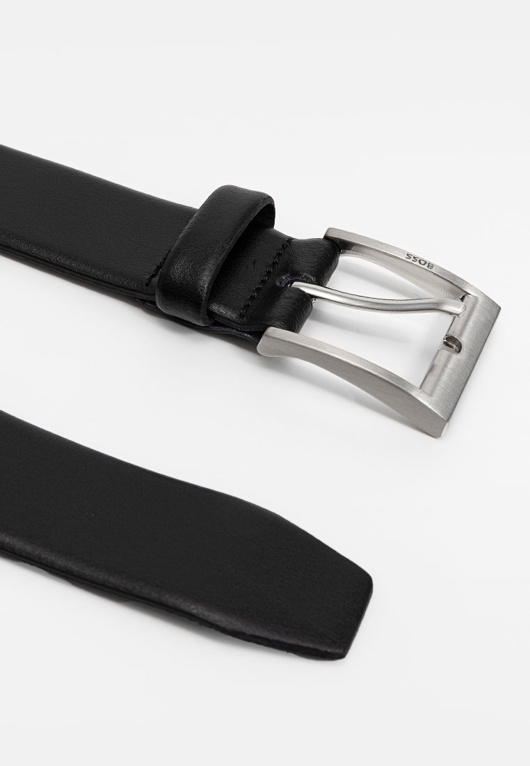 Ceinture en cuir noir avec une boucle en métal argenté brossé. La sangle présente une texture lisse et un design à bout effilé.