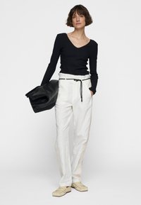 Zwarte geribbelde lange mouwen shirt, witte linnen broek met een taillekoord, en beige instappers, met een zwarte leren tas.