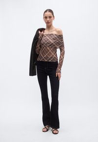 Top marrón de cuadros con escote off-the-shoulder, hecho de tela elástica, combinado con pantalones de mezclilla oscura y acampanados ajustados. Accesorios: chaqueta de cuero negra, sandalias.