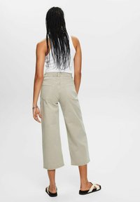 Jean beige clair à jambes larges avec une taille haute, doté de poches arrière, porté avec un débardeur blanc et des sandales noires. Texture en coton lisse.