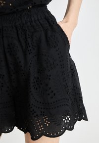Shorts noirs brodés avec un ourlet festonné, des motifs floraux et des poches latérales, dotés d'une ceinture élastique pour plus de confort.