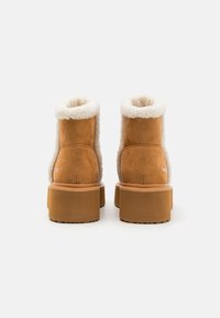 Beige ankelstøvler i ruskind med hvit plysjforing, kraftig beige plattformsåle og rund tå. Har minimal merkevare på siden.