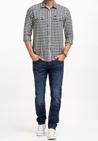 Czarna i biała koszula w kratkę gingham, z długimi rękawami, zapięcie na guziki, dwie kieszenie na piersi, połączona z niebieskimi dżinsami i białymi trampkami.