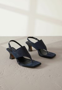 Marineblå ruskind slingback sko med T-bar design, firkantede tås og en afsmalnet hæl. Glat læder indersål og justerbar ankelrem.