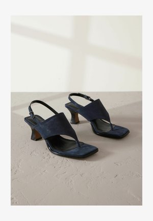 Navy suede avokkaat, joissa on T-mallinen nauha, neliön muotoiset varpaat ja kapeneva korko. Sileä nahkasisusta ja säädettävä nilkkahihna.