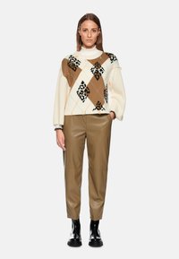 Knit sweater in cream with brown and black argyle pattern; ribbed cuffs and collar. Paired with brown leather pants and black ankle boots.
