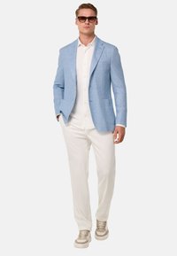 Blazer azul claro, camisa blanca, pantalones crema, zapatillas beige. El blazer tiene dos bolsillos y una tela texturizada.