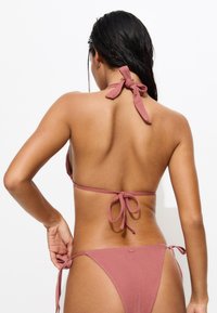 Bikini en tissu rose poussiéreux avec un col halter et un dos noué. Offre une couverture minimale avec des liens ajustables sur les côtés des bas.