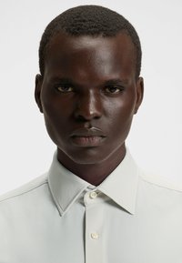 Camicia button-up in tessuto grigio chiaro con colletto strutturato e superficie texturizzata, dotata di bottoni rotondi e una vestibilità elegante e su misura.