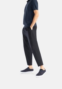 Marineblaues Poloshirt kombiniert mit schwarzen, taillierten Hosen und marineblauen Sneakern. Das Material wirkt weich; die Sneaker haben weiße Sohlen und beiges Akzentband.