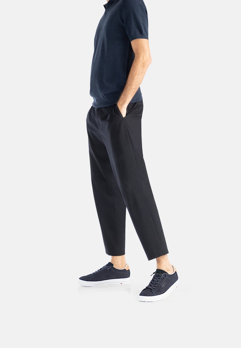 Marineblaues Poloshirt kombiniert mit schwarzen, taillierten Hosen und marineblauen Sneakern. Das Material wirkt weich; die Sneaker haben weiße Sohlen und beiges Akzentband.