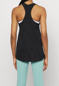 Débardeur noir sans manches avec un dos nageur et un détail froncé, associé à un legging bleu turquoise clair, vu de dos.