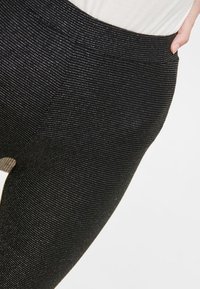 Svarta leggings med en texturerad, ribbad yta och resårmidja, delvis instoppade under en ljusfärgad topp.
