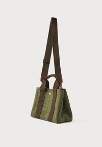 Μικρή πράσινη μάλλινη τσάντα tote με καφέ δερμάτινες λεπτομέρειες, διπλές χειρολαβές και ρυθμιζόμενη μακριά ιμάντα ώμου, κρεμάστηκε σε λευκό φόντο.