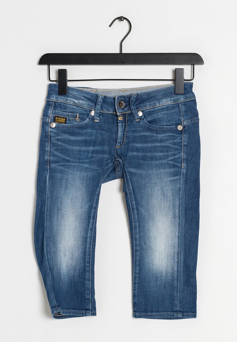 Jean capri en denim bleu suspendu à un cintre noir. Comprend cinq poches, une fermeture à boutons et un léger délavage du tissu.