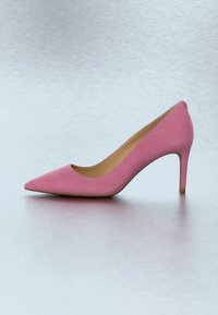 Vaaleanpunainen mokkanahkainen piikkikorkokenkä, jossa on terävä kärki, sileä pinta ja kapeneva korko. Ei näkyvissä koristeita tai kuvioita.