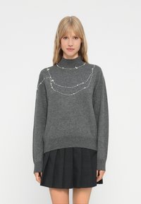 Pulover gri cu guler înalt, având accente decorative din perle dispuse într-un model curbat pe piept. Textură moale, croială lejeră.
